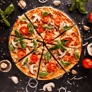 A delicious pizza topped with fresh tomatoes, mushrooms, basil, and cheese, sliced into eight pieces on a dark slate board. Surrounding the pizza are scattered ingredients like garlic cloves, basil leaves, tomatoes, mushrooms, and onion rings, set against a black background with salt and cheese shavings, evoking a rustic, appetizing vibe.